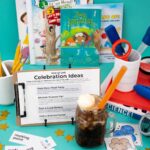 A root beer float with an orange straw in front of a stack of books and a lesson plan.